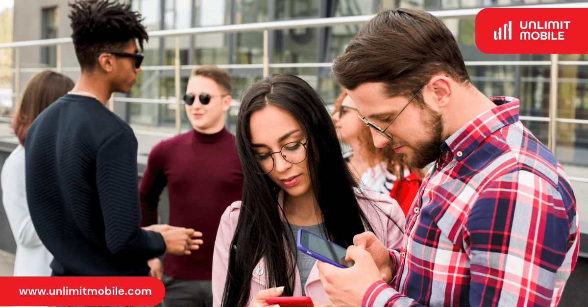 A group of students outside a campus building, two of them looking at a phone together