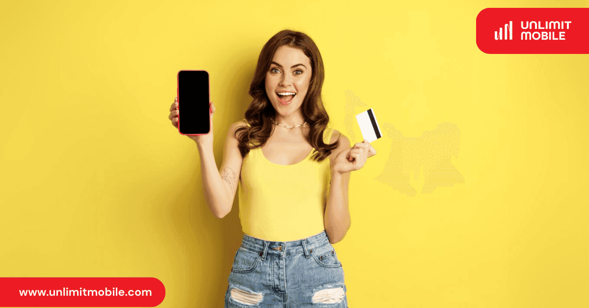 A smiling young woman holding up a smartphone in one hand and a payment card in the other